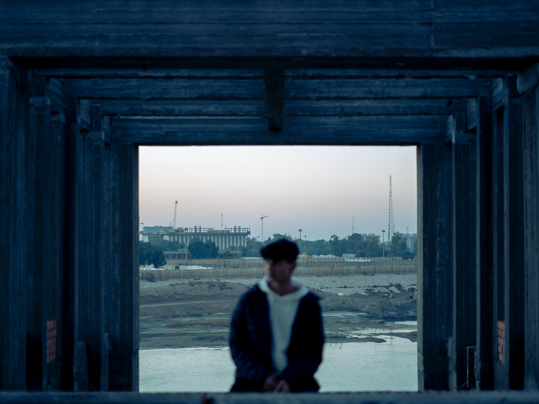 man standing behind a wooden window frame and industrial landscape in background